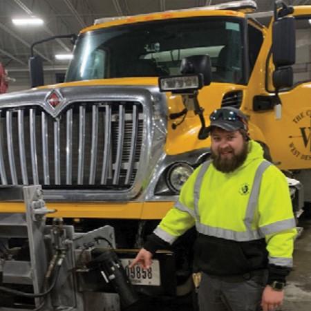 Road maintenance worker in front of snowplow vehicle